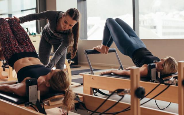 Mujeres haciendo pilates en máquinas para disfrutar de sus beneficios.